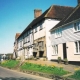 Old half-timbered houses and white cottages line a village street on a sunny day with daffodils in flower.