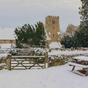 A snow-covered picnic table and gate with a church and trees in the background