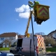 A worker in a lift repairs a streetlamp next to a utility van on a suburban road.