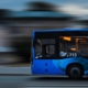 a blue bus driving down a street next to a tall building